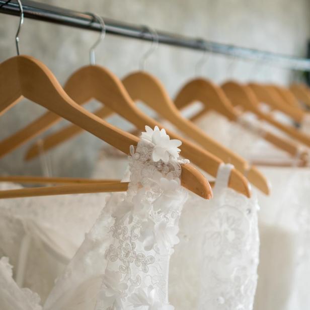 Mehrere weiße Brautkleider hängen an hölzernen Kleiderbügeln.