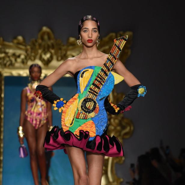 Ein Model präsentiert ein farbenfrohes Kleid in Gitarrenform auf einem Laufsteg.
