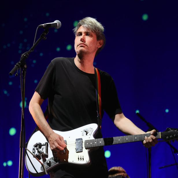 Ein Mann mit grauen Haaren spielt auf einer weißen Deimel Gitarre auf der Bühne.