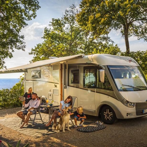 Eine Familie entspannt mit Hund vor ihrem Wohnmobil auf einem Campingplatz in Küstennähe.