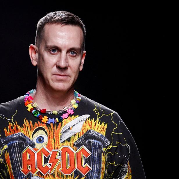 Ein Mann mit einem AC/DC-T-Shirt und einer bunten Halskette vor schwarzem Hintergrund.