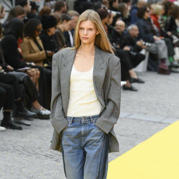 Ein Model präsentiert ein Outfit mit übergroßem Blazer und Jeans mit Reißverschlüssen auf dem Laufsteg.