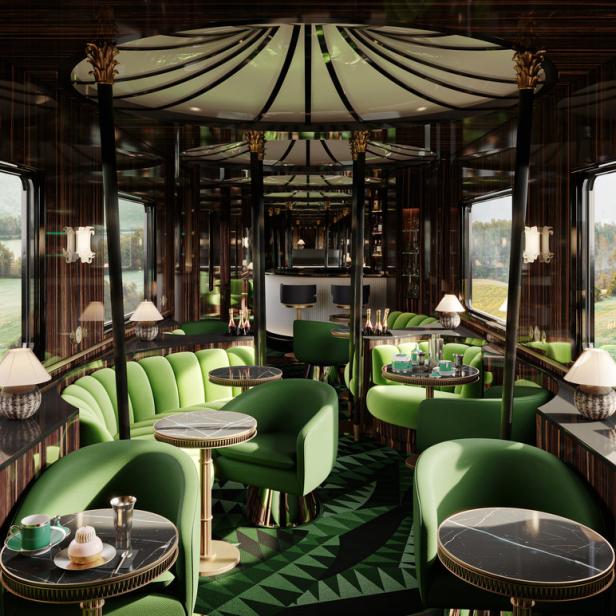 Der luxuriöse Salonwagen eines Zuges mit grünen Sitzen und einer Bar im Hintergrund.