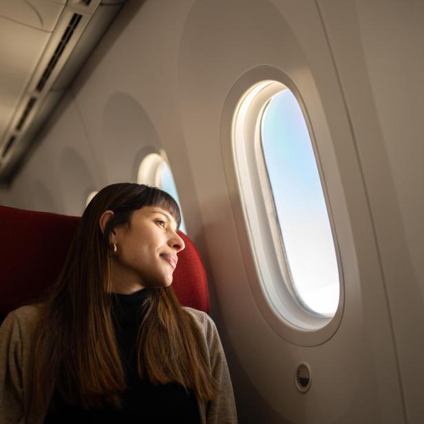 Junge Frau, die mit dem Flugzeug reist und aus dem Fenster schaut.