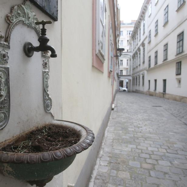 Ein alter Brunnen an einer Hauswand in einer Gasse.