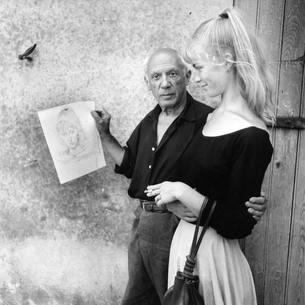 Pablo Picasso mit einer jungen Frau und einer Porträtzeichnung in der Hand.