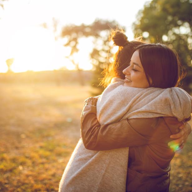 Zwei Frauen umarmen sich in einem Park bei Sonnenuntergang.