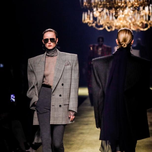 Models präsentieren übergroße Blazer auf dem Laufsteg unter einem Kronleuchter.
