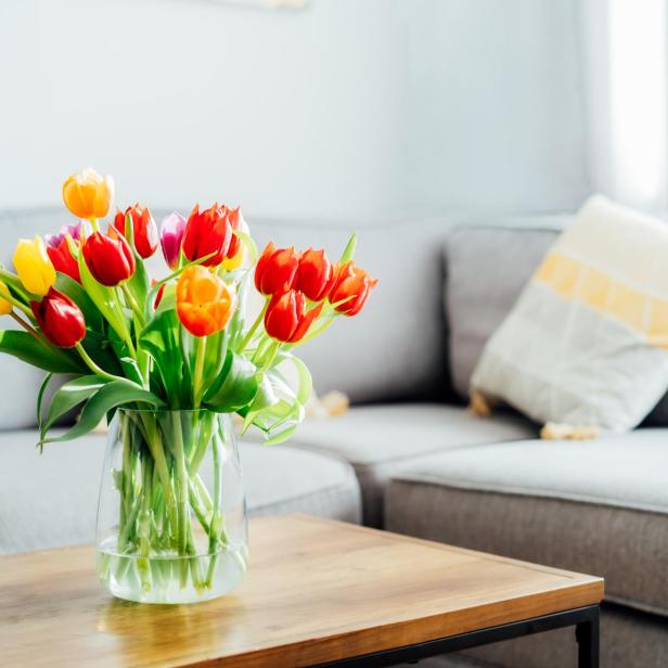 Ein bunter Tulpenstrauß steht auf einem Holztisch vor einem grauen Sofa.
