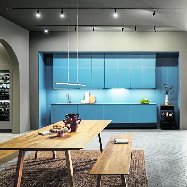 Ein Esszimmer mit einem Holztisch und einer blauen Küchenzeile im Hintergrund.