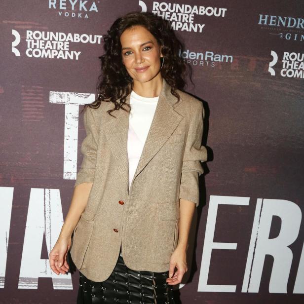 Katie Holmes posiert vor einer Wand mit Theaterplakaten.