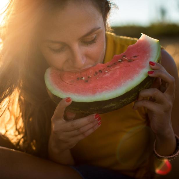 Junge Frau isst im Freien ein Stück Wassermelone.
