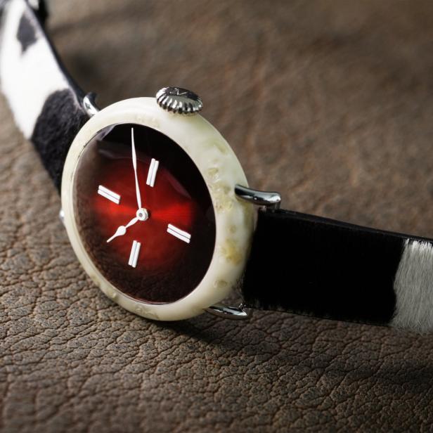 Eine Armbanduhr mit einem rotbraunen Zifferblatt und einem Armband aus Kuhfell liegt auf Leder.