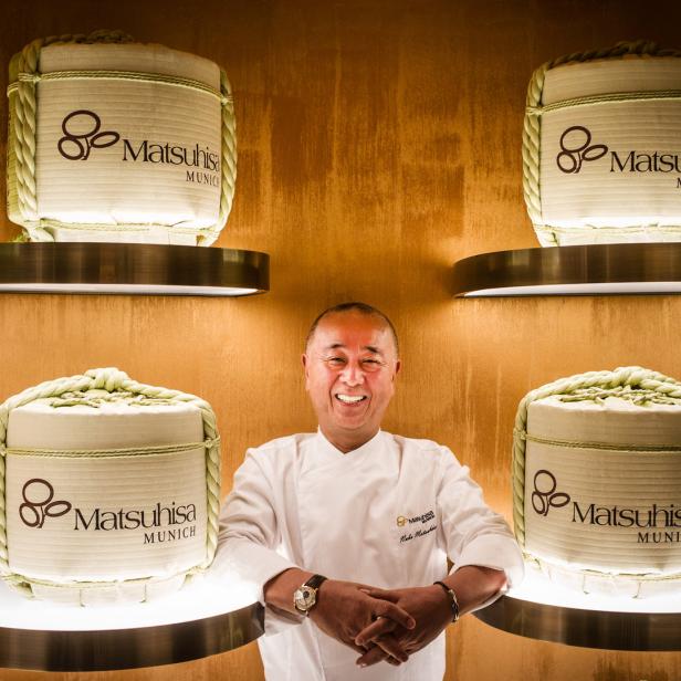 Nobu Matsuhisa, Gründer des Restaurants Matsuhisa München, posiert vor Dekorationsobjekten mit dem Logo des Restaurants.