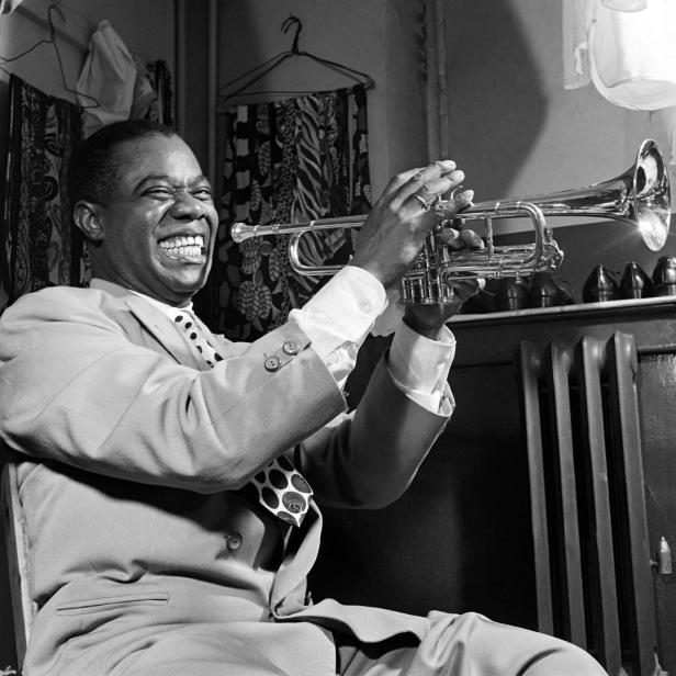 Louis Armstrong spielt Trompete und lächelt.