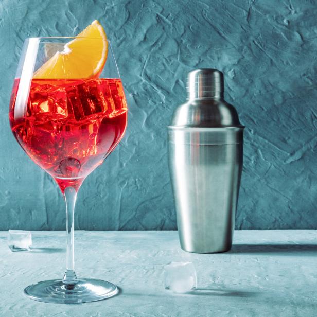 Ein Aperol Spritz mit einer Orangenscheibe und einem Cocktailshaker.