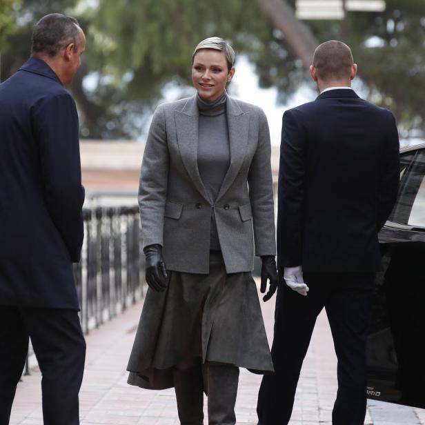 Fürstin Charlène von Monaco mit kurzem, blonden Haar und grauem Kostüm vor einem Auto.