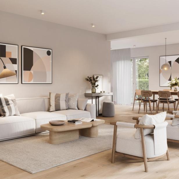 Ein helles Wohnzimmer mit Sofa, Sesseln und einem Essbereich im Hintergrund.