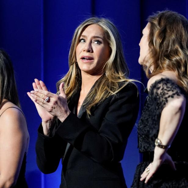 Jennifer Aniston klatscht neben zwei Frauen auf einer Bühne.