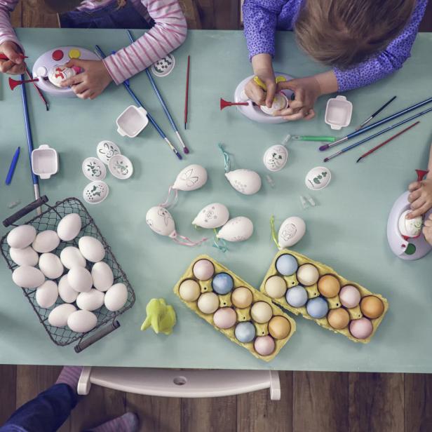 Kinder bemalen Ostereier an einem Tisch mit Farben und Pinseln.