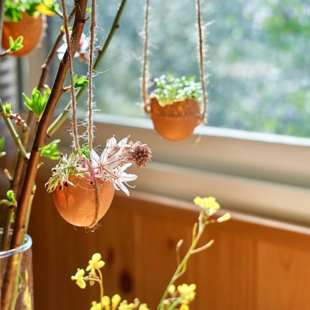 Dekorative Ostereier mit Pflanzen und Blumen hängen vor einem Fenster.