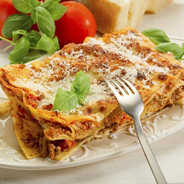 Ein Teller mit einem Stück Lasagne, garniert mit Basilikum und Parmesan.