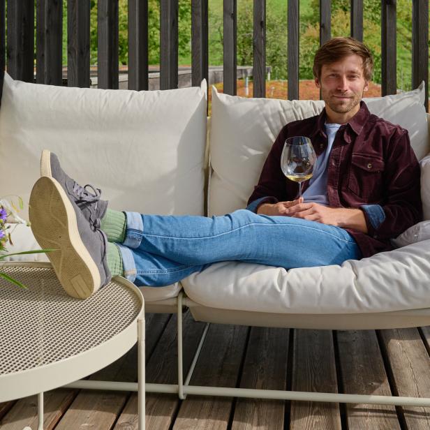 Ein Mann entspannt mit einem Glas Wein auf einer Couch im Freien.