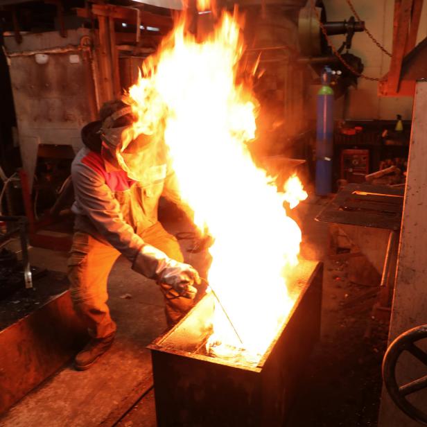 Ein Arbeiter mit Schutzkleidung hantiert mit einer Stichflamme in einer Werkstatt.