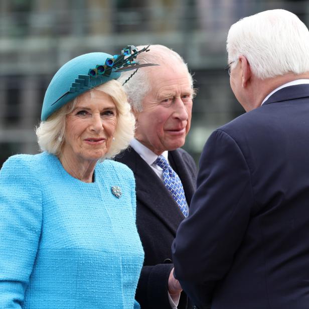 König Charles und Königin Camilla bei einem Treffen mit einem Mann in einem dunklen Anzug.