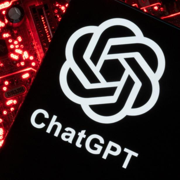 Das ChatGPT-Logo auf einem Smartphone, das vor einer rot beleuchteten Computerplatine liegt.