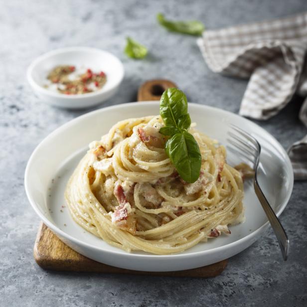 Ein Teller Spaghetti Carbonara, garniert mit einem Basilikumblatt.