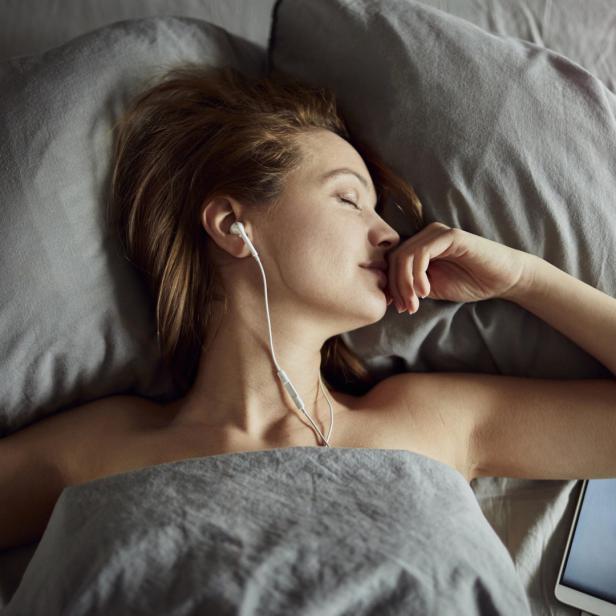 Eine Frau liegt mit Kopfhörern im Bett und schläft.