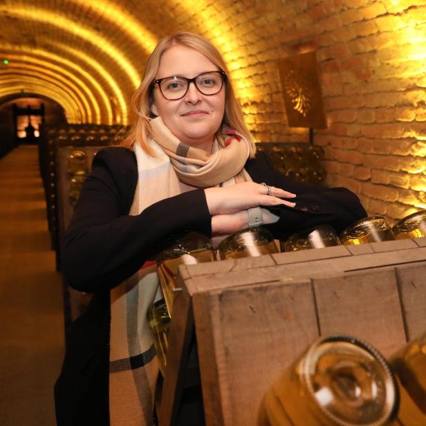 Eine Frau steht in einem Weinkeller vor Regalen mit Weinflaschen.