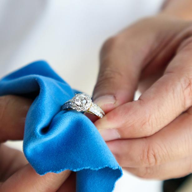 Eine Person reinigt einen Diamantring mit einem blauen Tuch.