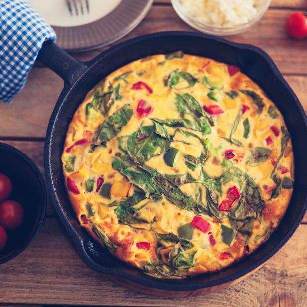 Eine Frittata mit Gemüse in einer gusseisernen Pfanne auf einem Holztisch.
