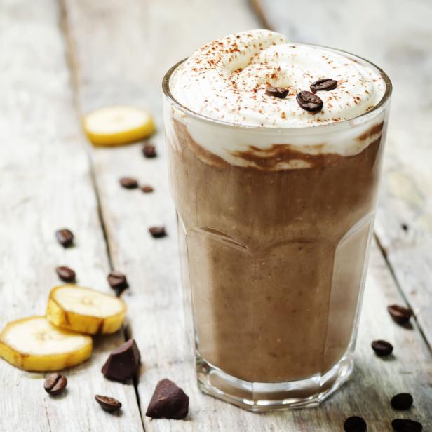 Ein Schokoladen-Bananen-Smoothie mit Schlagsahne und Kaffeebohnen auf einem Holztisch.