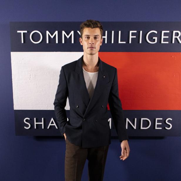 Shawn Mendes posiert vor einem Tommy Hilfiger-Logo.