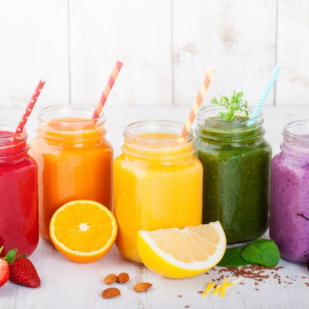 Fünf Gläser mit bunten Smoothies und Strohhalmen stehen auf einem Tisch.