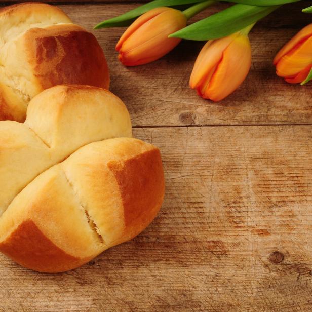 Zwei Brioche-Brote und drei orangefarbene Tulpen auf einem Holztisch.