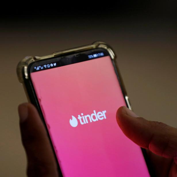 Eine Hand hält ein Smartphone mit der geöffneten Tinder-App.