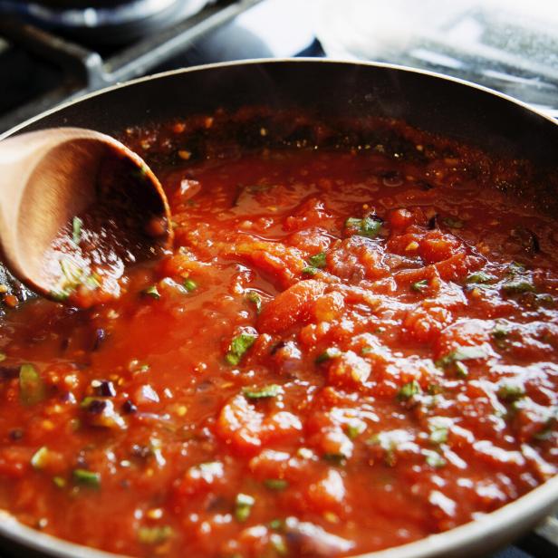 Eine Tomatensauce köchelt in einer Pfanne auf dem Herd.