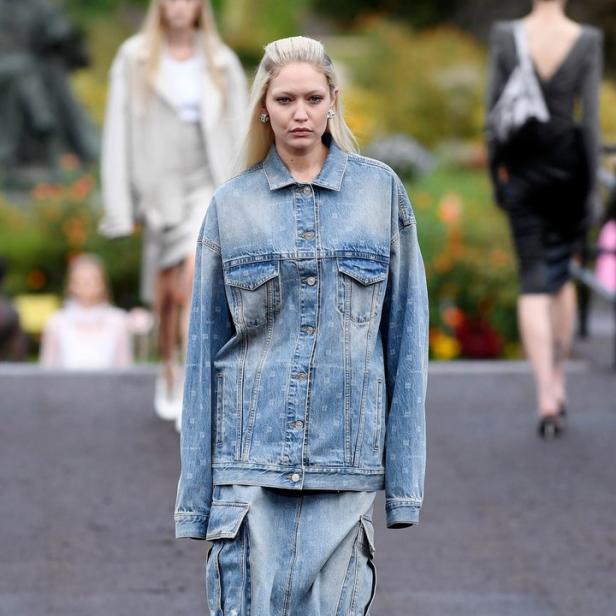 Ein Model in Jeansjacke und Rock mit Cargotaschen auf einem Laufsteg.