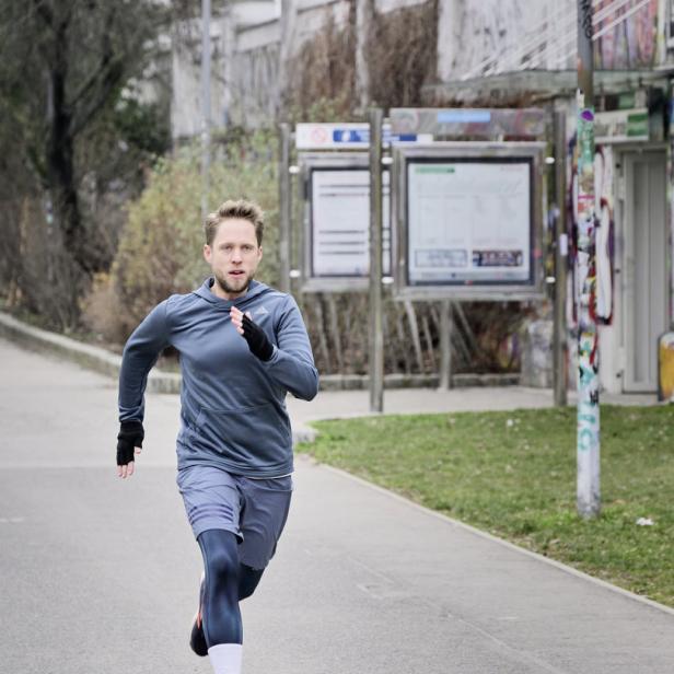 Ein Mann joggt auf einer Straße an einer Bushaltestelle vorbei.