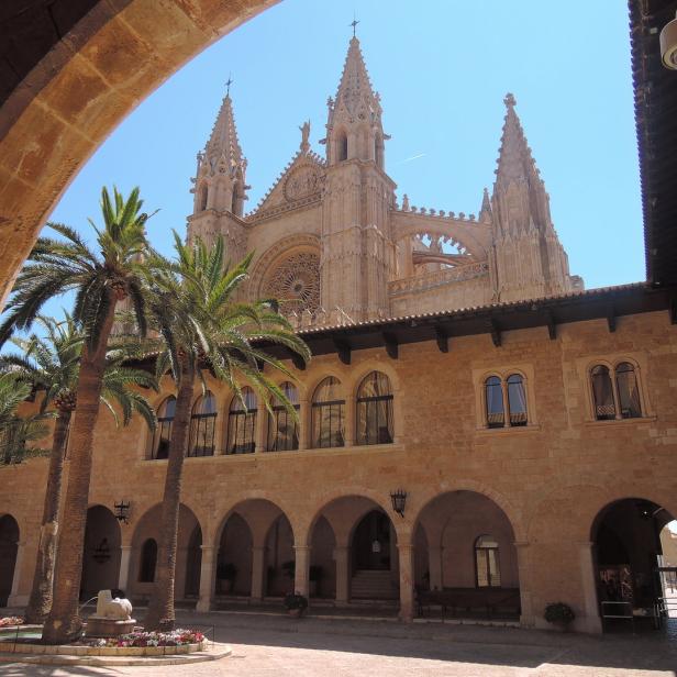 Blick durch einen Torbogen auf die Kathedrale von Palma mit Palmen im Innenhof.