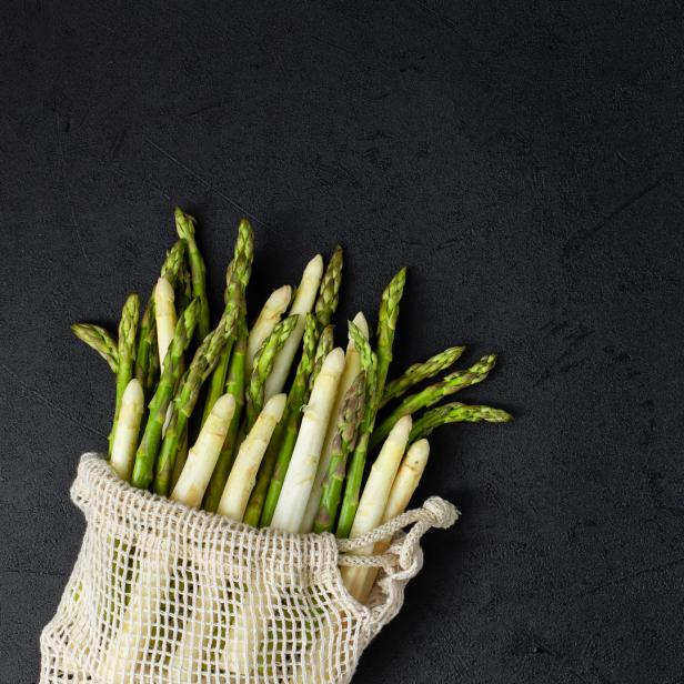 Grüner und weißer Spargel in einem Stoffbeutel auf schwarzem Hintergrund.