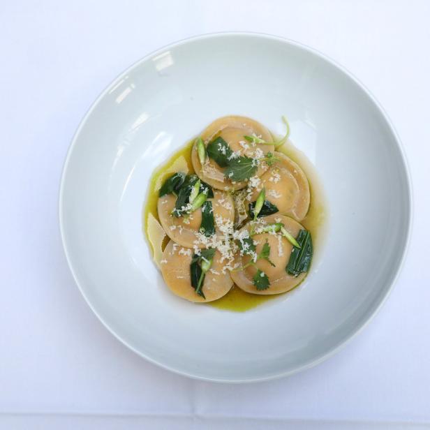 Ein Teller mit Ravioli, garniert mit Kräutern und geriebenem Käse.