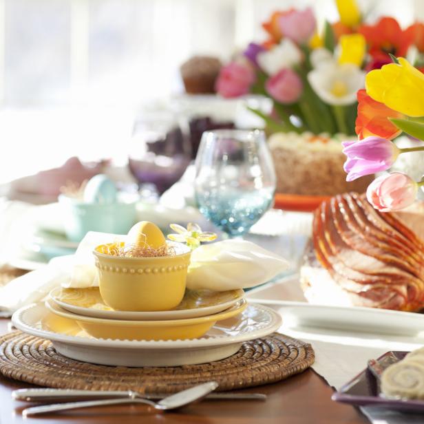 Ein festlich gedeckter Tisch mit Osterschinken, Tulpen und bunten Eiern.