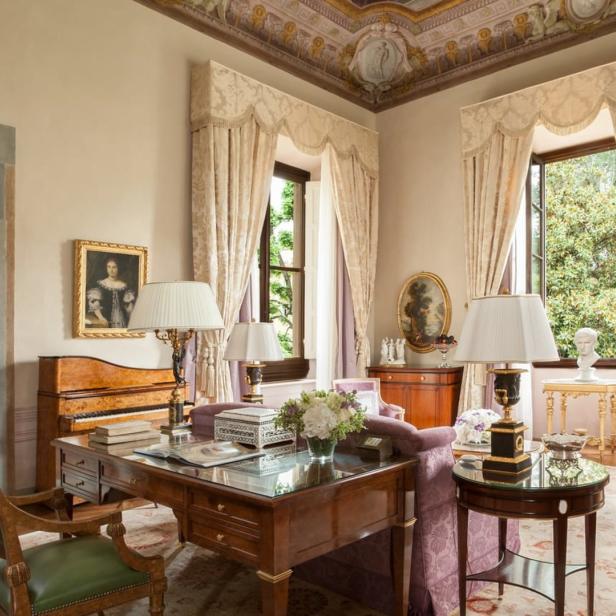 Ein elegantes Arbeitszimmer mit antiken Möbeln, Gemälden und einem Schreibtisch mit Glasplatte.