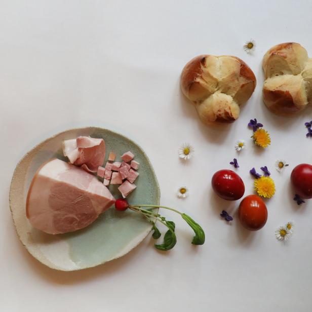 Ein Teller mit Schinken, Krainerwurst, Eiern und Osterbrot, dekoriert mit Blumen.