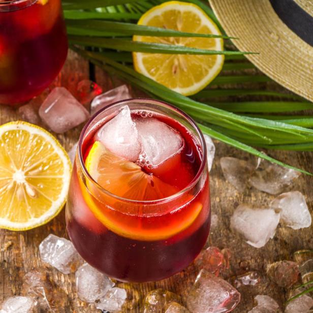 Zwei Gläser Sangria mit Eis und Zitronenscheiben auf einem Holztisch.